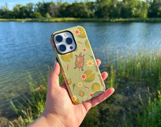 The pond life phone case held in front of a pond.
