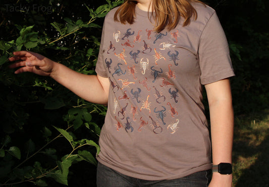 Another view of a woman wearing the scorpion unisex t-shirt in the color "pebble".