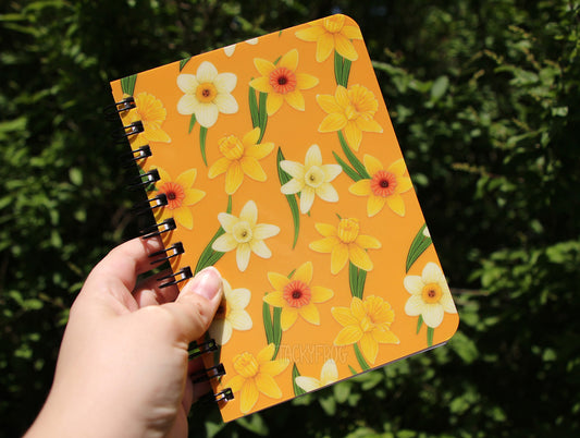 The yellow daffodil spiral bound mini journal held up in the air.