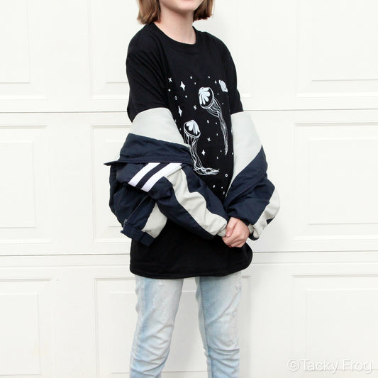 A young woman wearing a t-shirt with space jellyfish on it. She is also wearing a jacket off her shoulders.