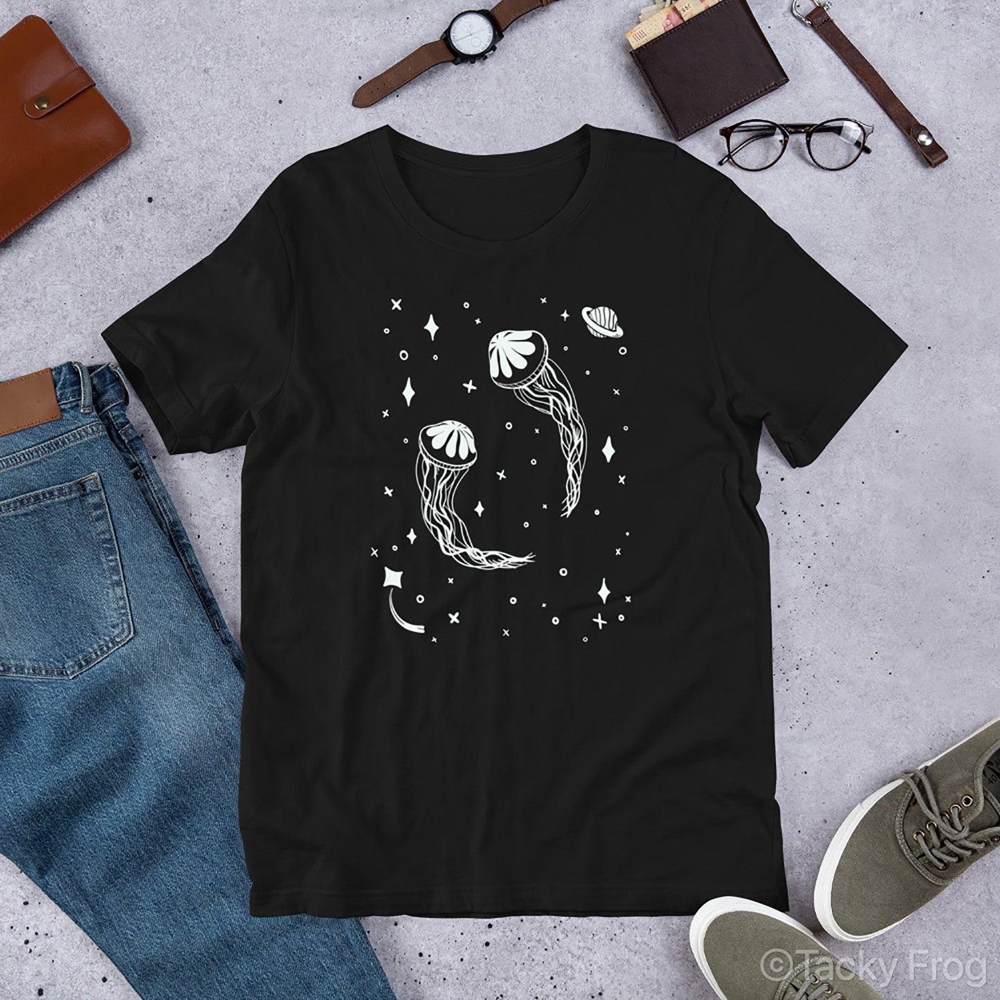 A mockup of the black space jellyfish shirt placed next to clothes and accessories.