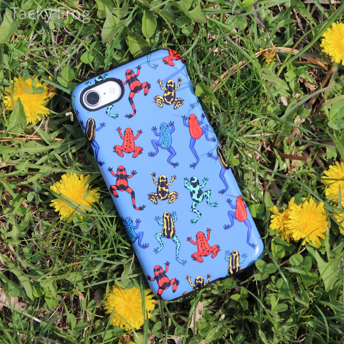 The blue dart frog phone case placed in the grass with dandelions.