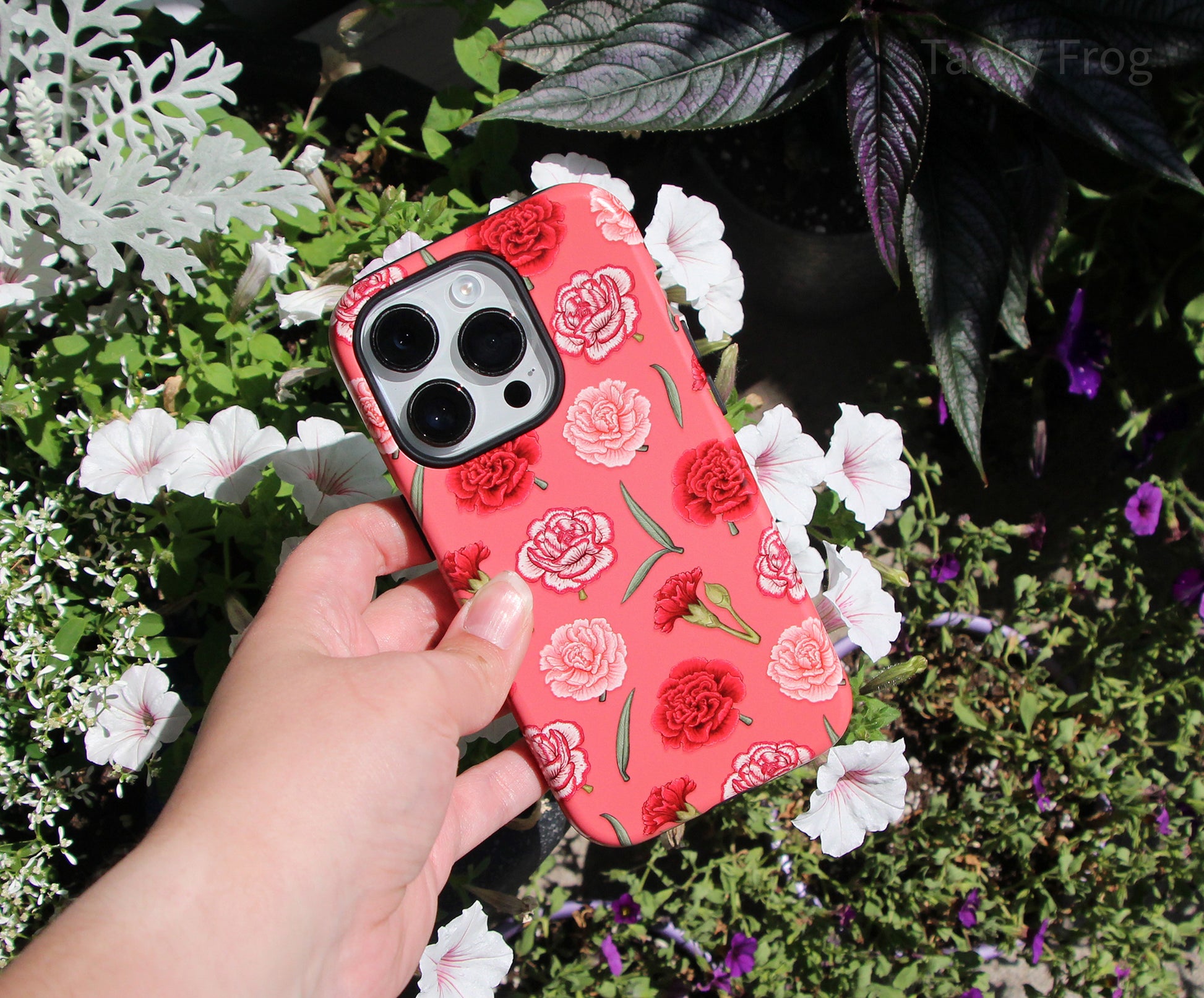 The red and pink carnations phone case held in front of flowers.