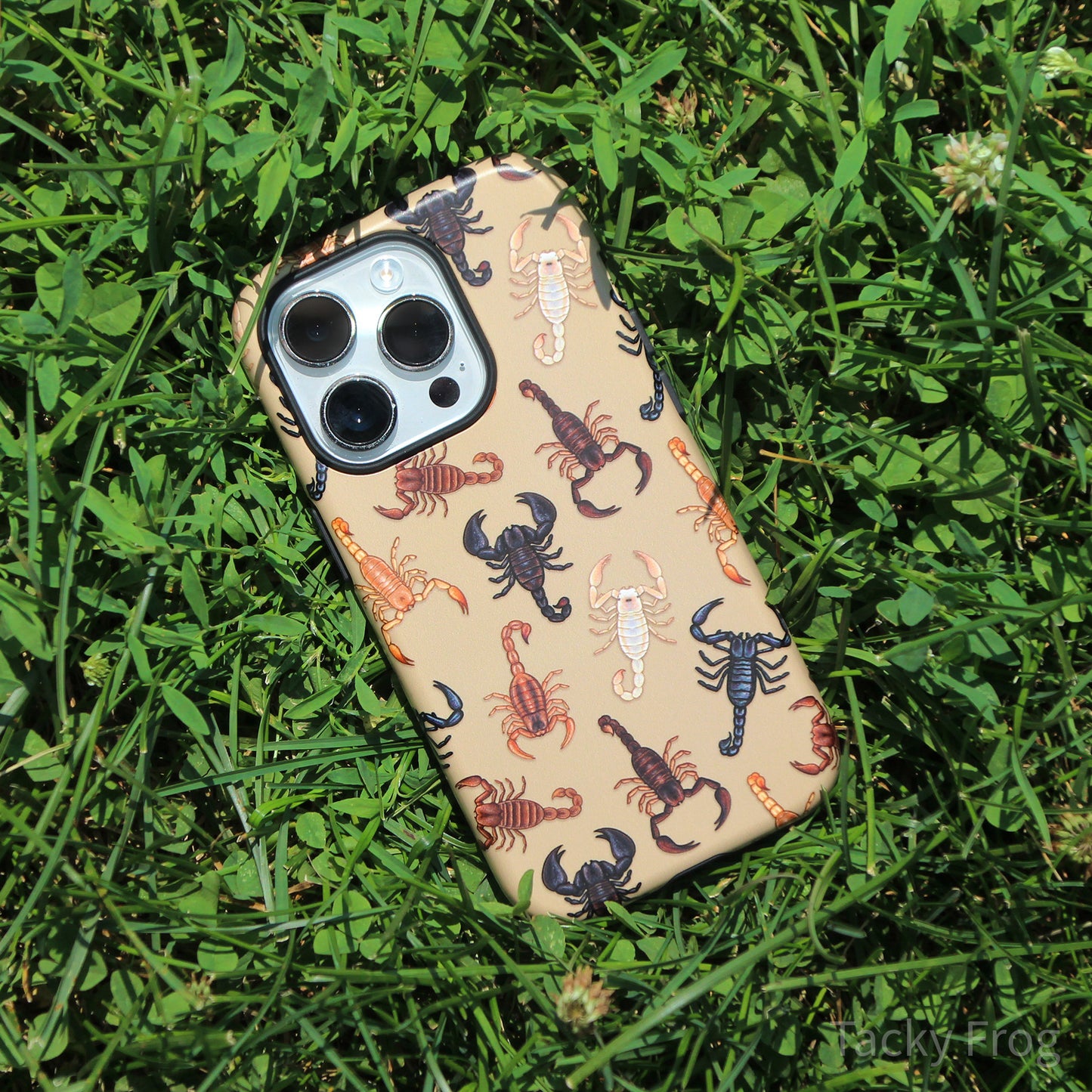 The scorpion-patterned phone case placed on some grass.