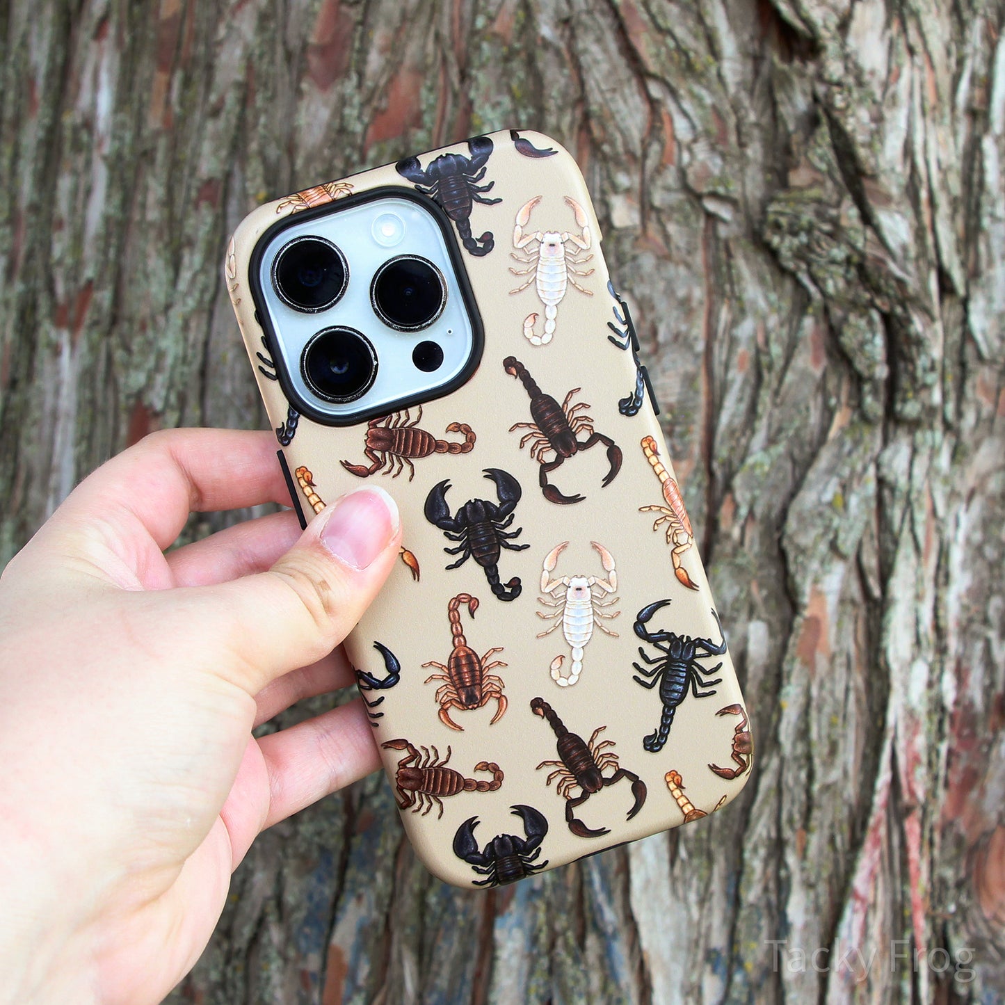 The scorpion-patterned phone case held up in front of a tree.