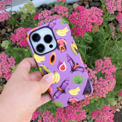 The fruit bats tough phone case held over some pink flowers.