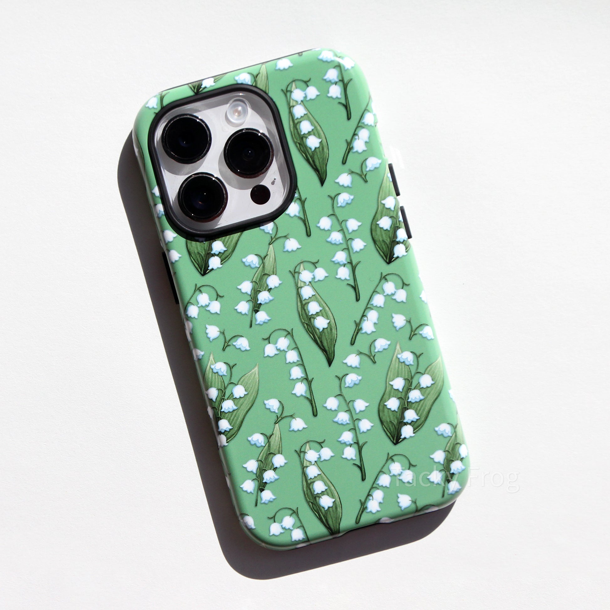 A green phone case featuring a pattern of lilies of the valley and leaves.