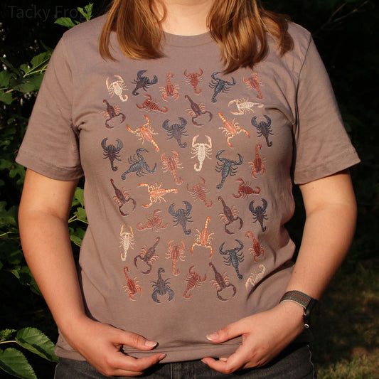 A woman wearing a t-shirt with various scorpions on it in the color variant "pebble". The photo was taken at sunset, so there is a warm glow to it.