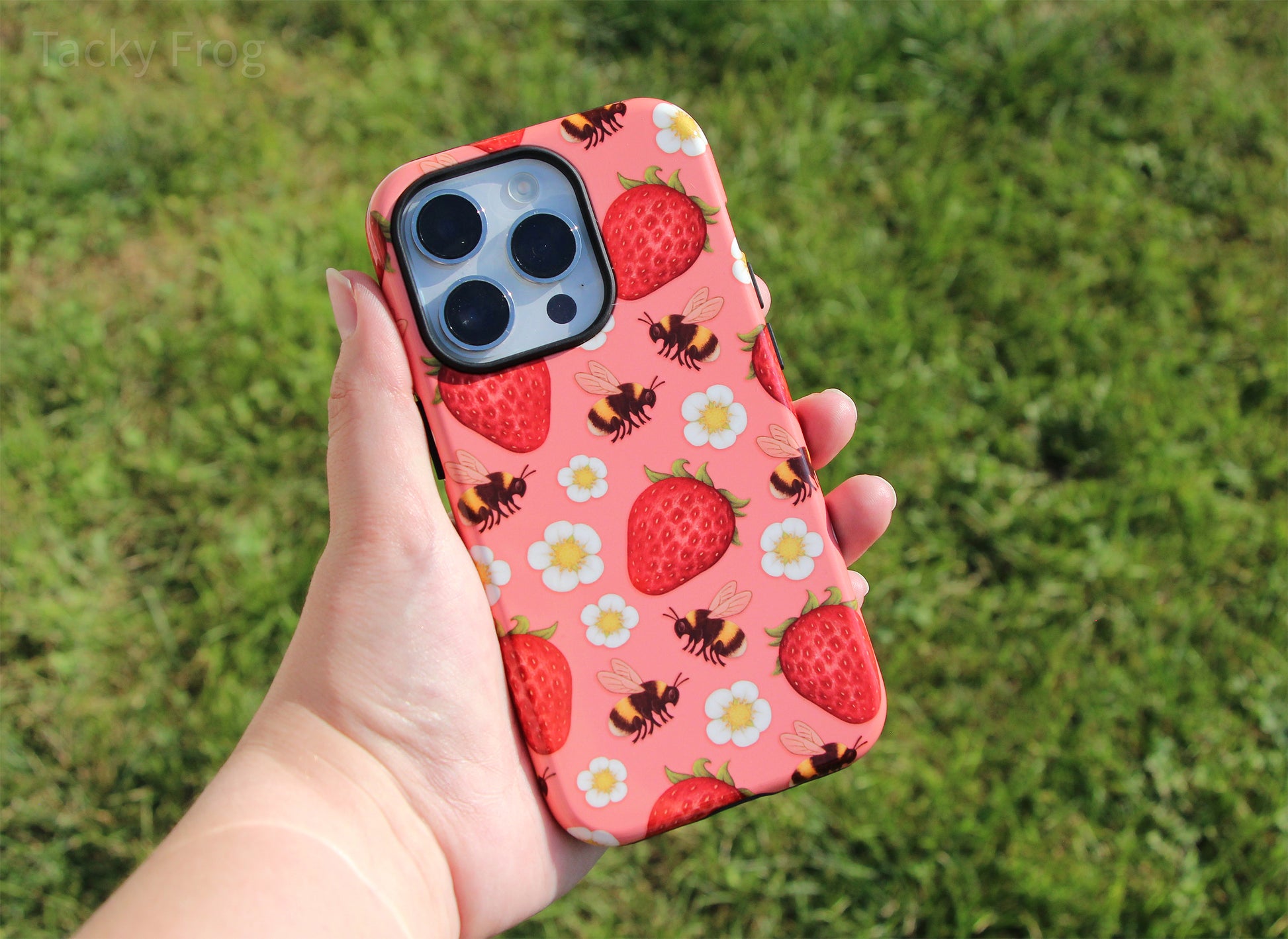 The strawberries and bees phone case held over some grass.