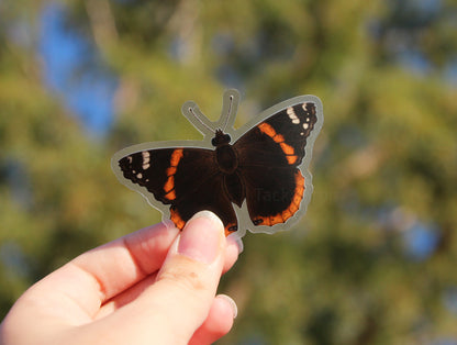 The red admiral butterfly clear vinyl sticker held up in front of a tree.