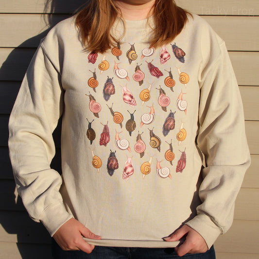 A woman wearing the snails sweatshirt in the color "sand". The photo was taken during sunset, so there is a warm glow on the shirt.