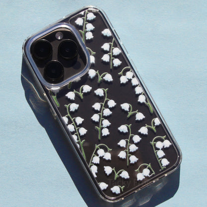 A clear phone case, shown on a dark phone, that features a pattern of white lily of the valley flowers.