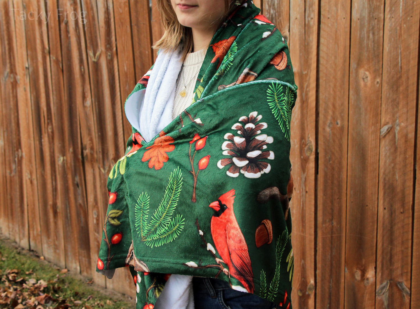 The winter foraging blanket wrapped around a young woman. This lightweight blanket features a colorful, high quality pattern on one side and a solid white opposite side.