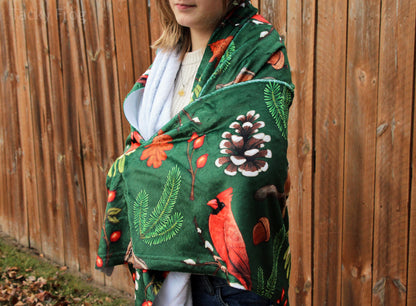 The winter foraging blanket wrapped around a young woman. This lightweight blanket features a colorful, high quality pattern on one side and a solid white opposite side.