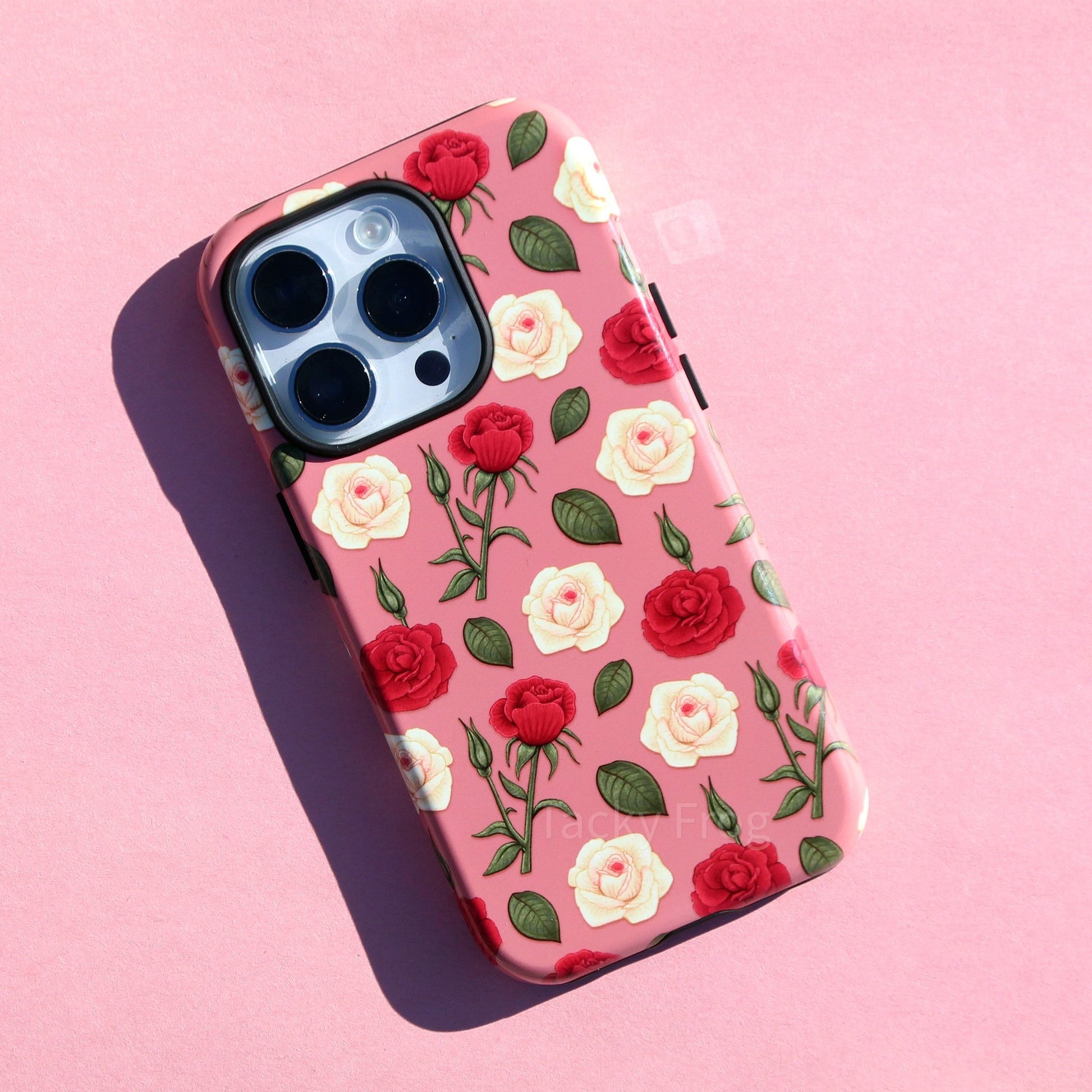 A pink phone case featuring a pattern of dark pink and cream-colored roses and green vegetation.