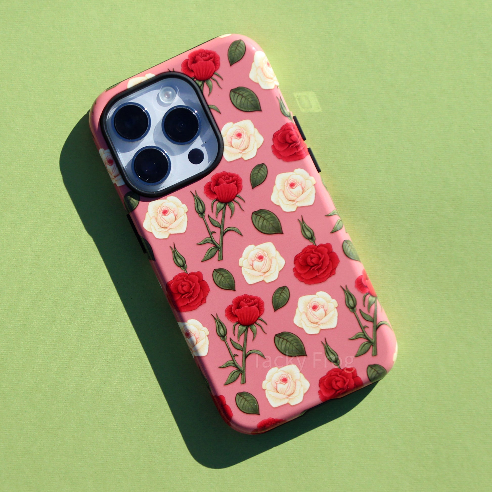 A pink phone case featuring a pattern of dark pink and cream-colored roses and green vegetation.