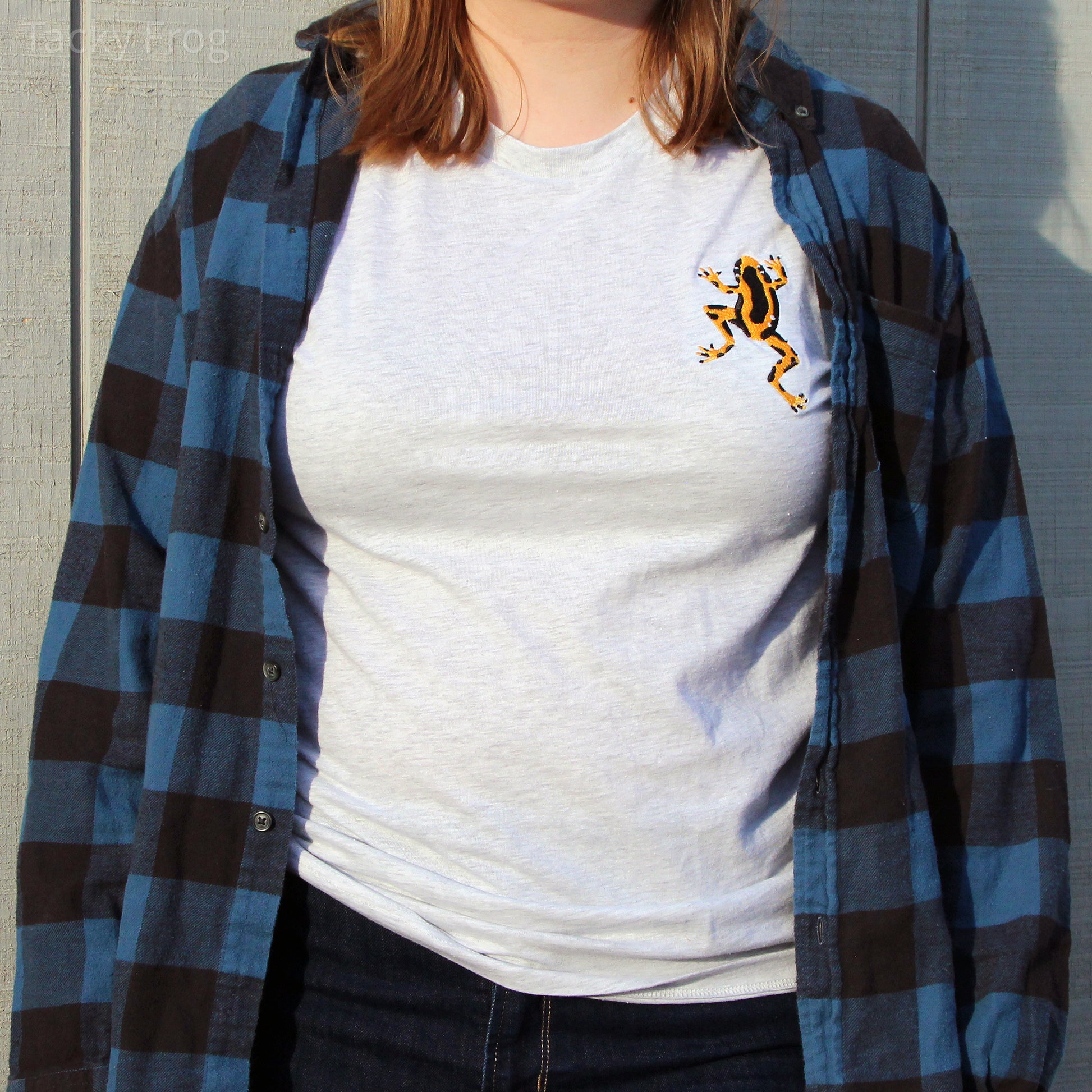 A woman wearing the yellow dart frog embroidered shirt, in the "ash" variant, under a blue flannel.