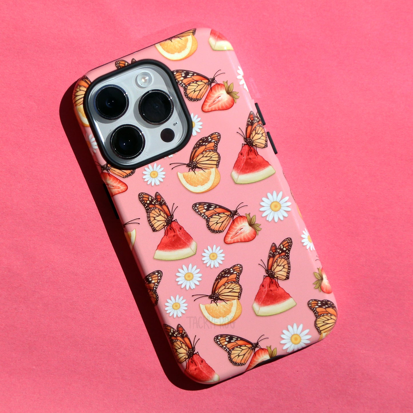 A pink phone case featuring a pattern of daisies and monarch butterflies on watermelon, lemons, and strawberries