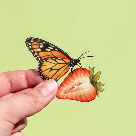 A clear vinyl sticker of a monarch butterfly on a strawberry.