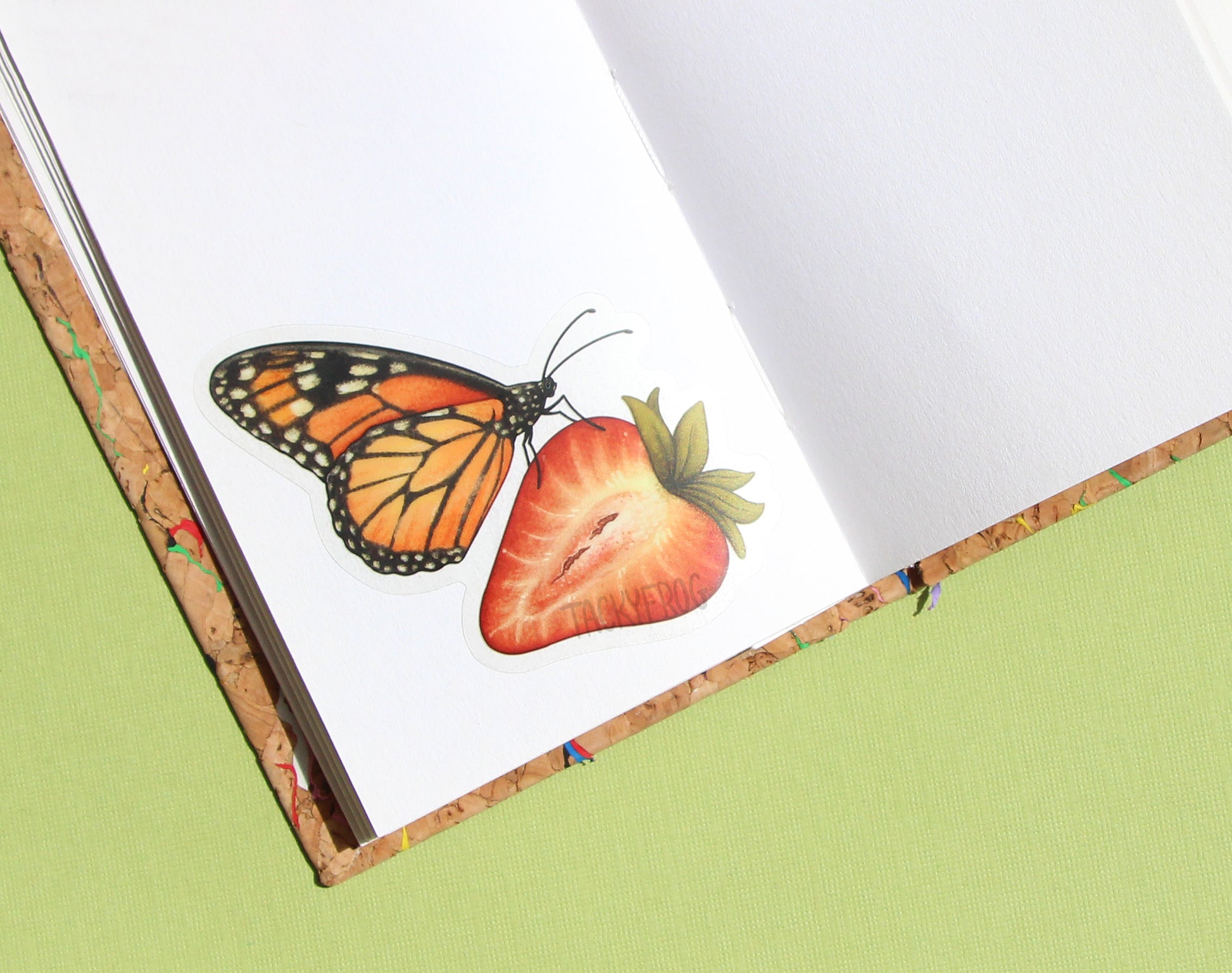 The monarch butterfly on a strawberry sticker placed in a sketchbook.