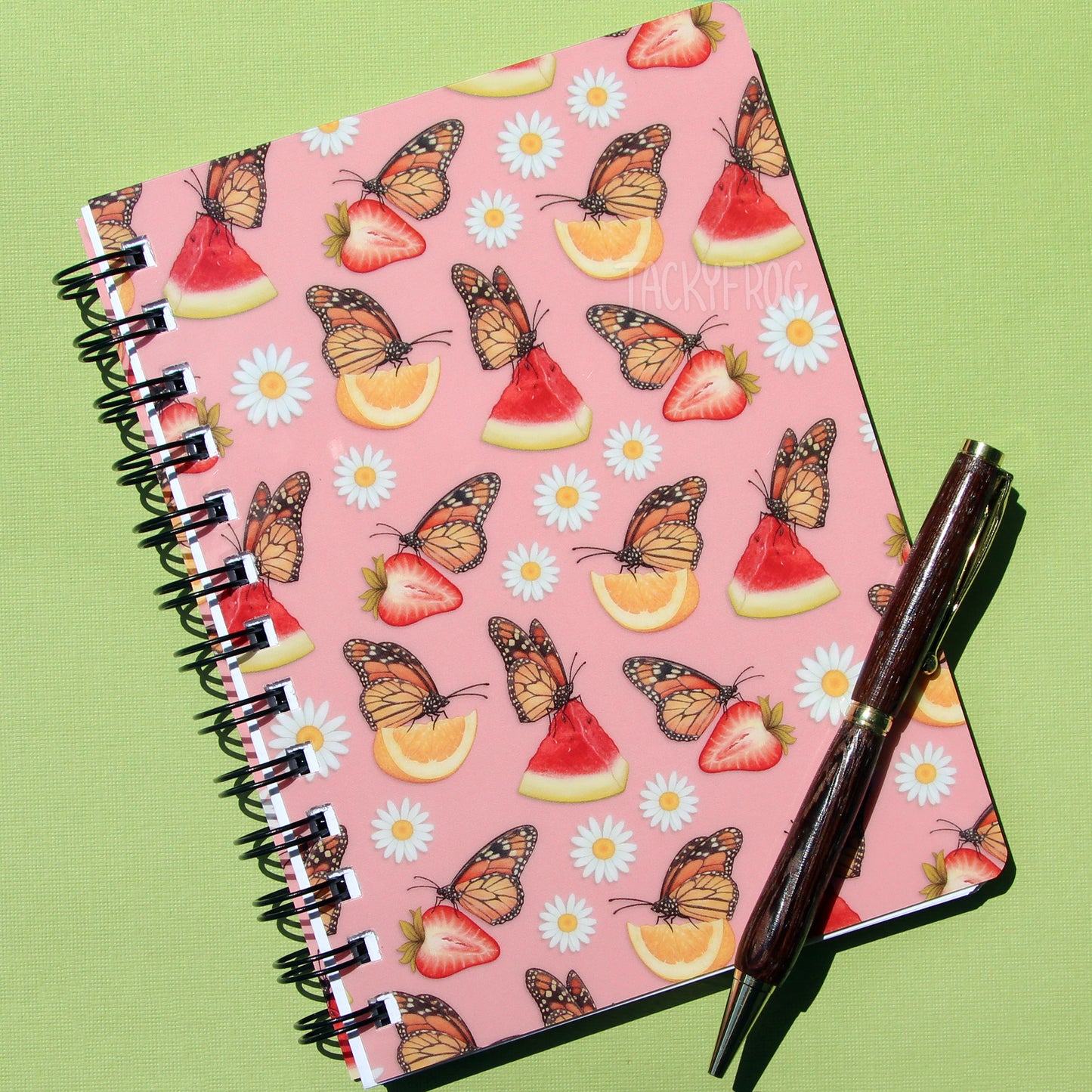 The hungry monarch butterfly notebook with a pen placed on top of it. The pen is not included.