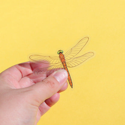 A clear vinyl sticker of an orange dragonfly.