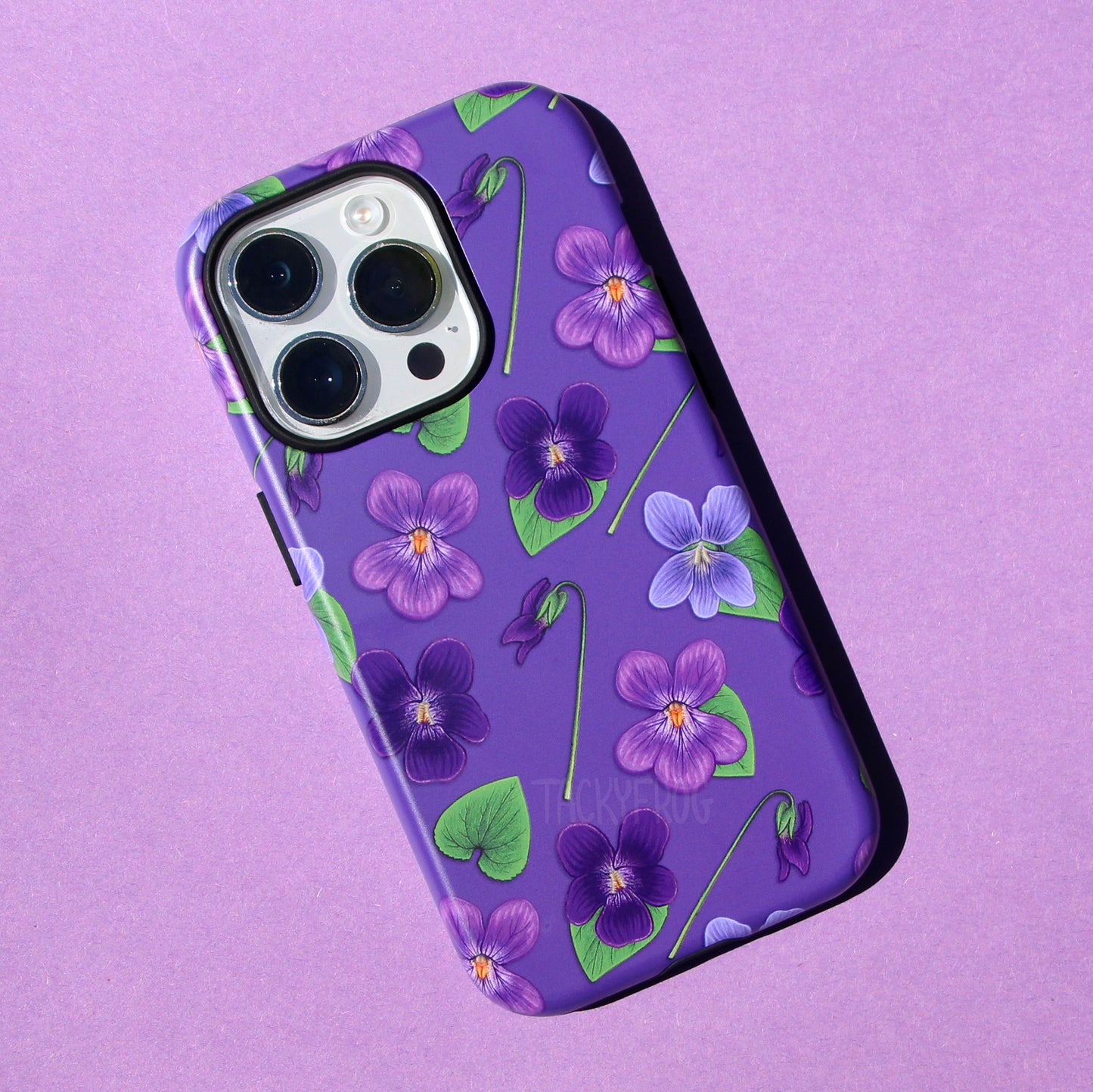 A purple phone case featuring a pattern of violet flowers and green leaves. The case is dual-layered, with the inner layer being solid black.