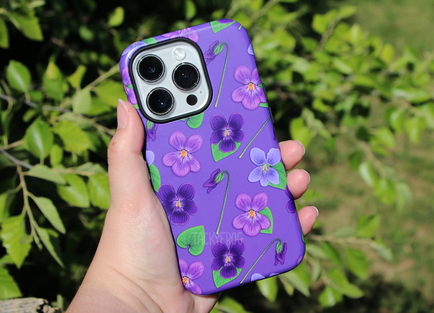 The violet-pattern phone case held in front of a tree.