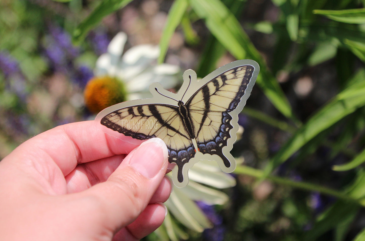 The yellow swallowtail butterfly clear vinyl sticker held above some flowers.