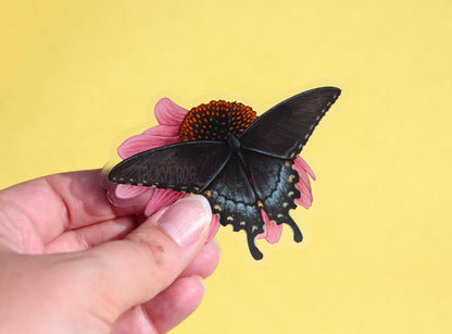 The swallowtail butterfly on coneflower sticker in front of a yellow background.