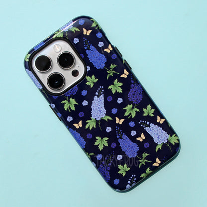 A dark blue phone case featuring a pattern of green leaves, yellow butterflies, and a few different shades of blue larkspurs. The case is dual layered. The inner layer is solid black.