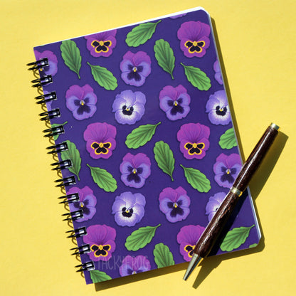 The purple pansy notebook against a yellow background. The pen is not included.