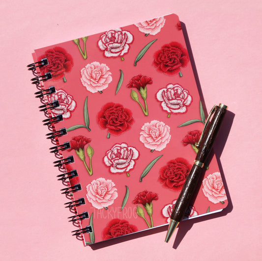 A pink notebook featuring a pattern of green leaves and pink, red, and white carnations.