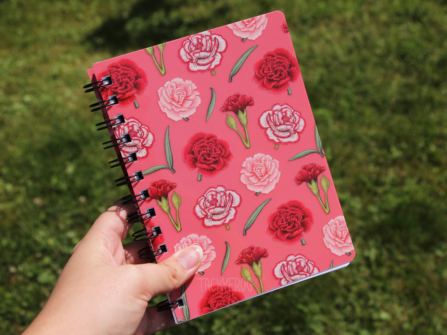 The carnation-patterned notebook held over some grass.