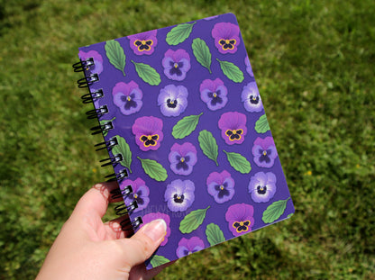 Purple pansy notebook held above some grass.