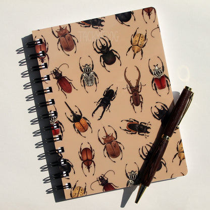 A muted brown notebook featuring a cover with beetles on it. The pattern features stag beetles, Goliath beetles, Hercules beetles, and more. The pen is not included.