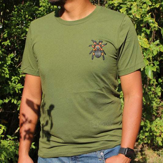 A man wearing an olive green-colored t-shirt with a red-knee tarantula machine embroidered on the shirt's left chest.