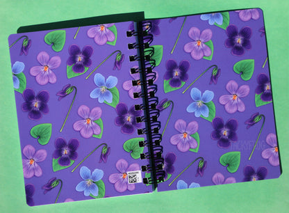 The back and front covers of the violet-patterned notebook. Please note that there is a small QR code in the bottom right corner of the back cover for warehouse purposes.