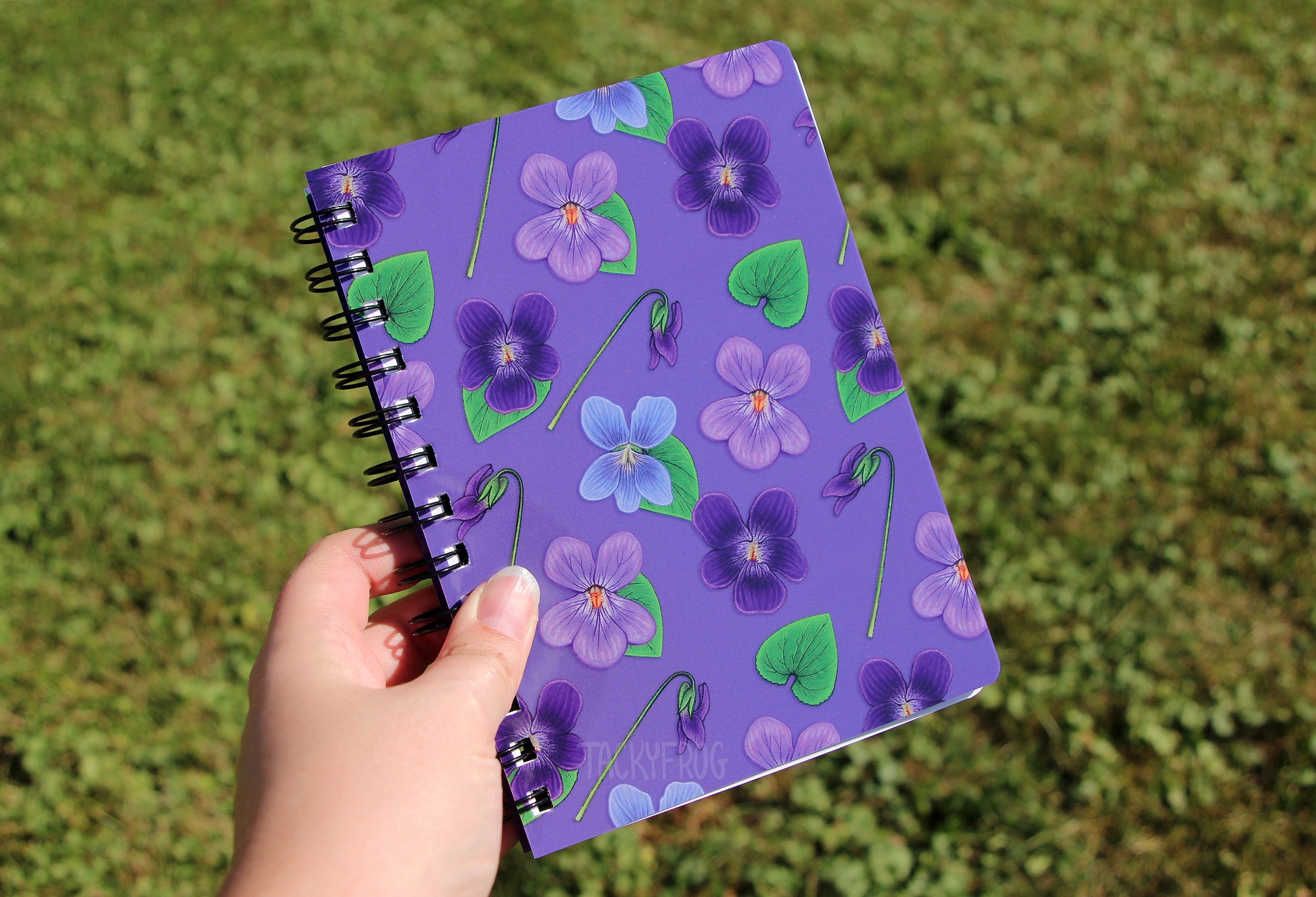 The 5 x 7 inch violet-patterned notebook held over grass.