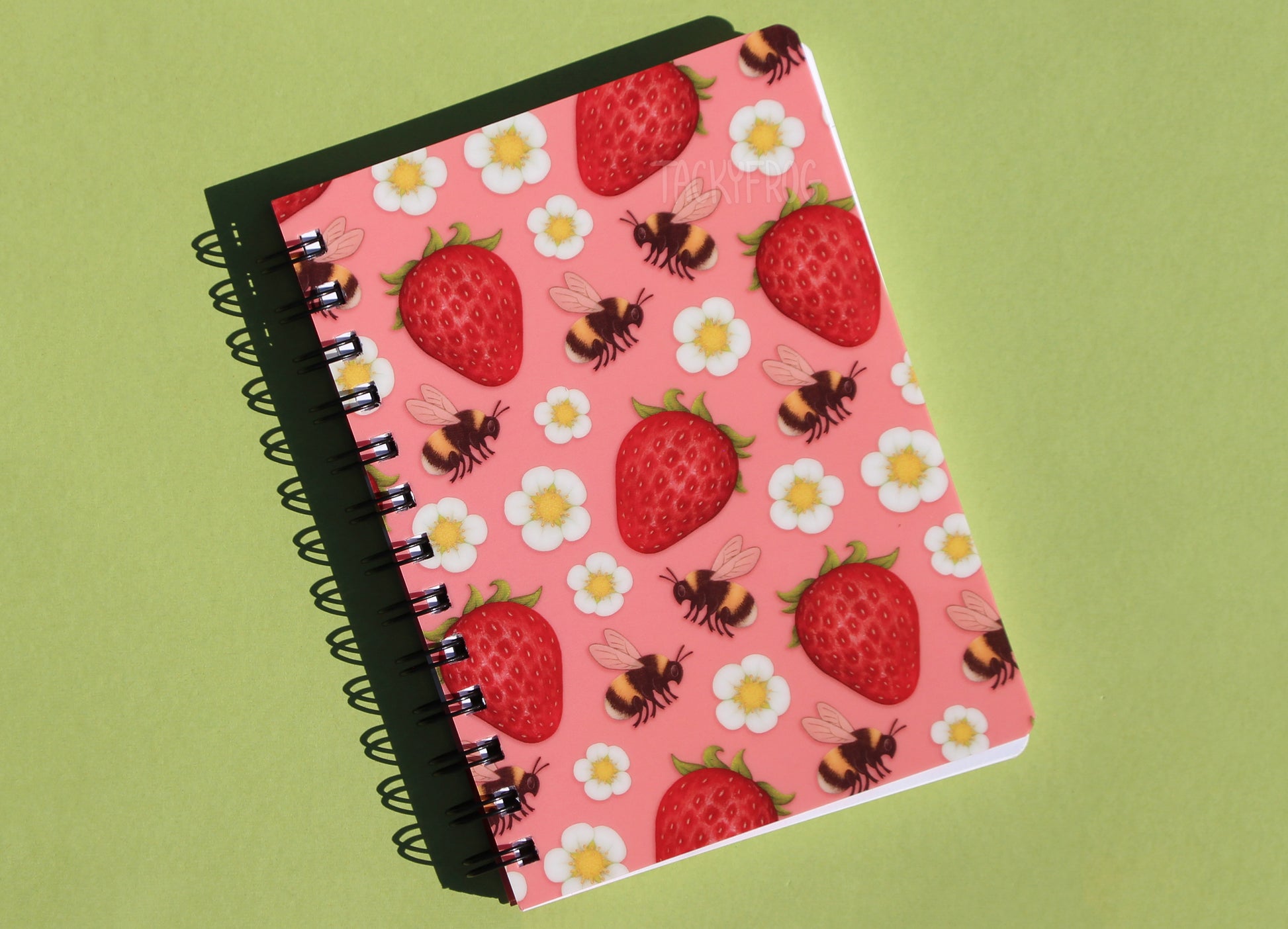 The strawberries and bees-patterned notebook against a green background.