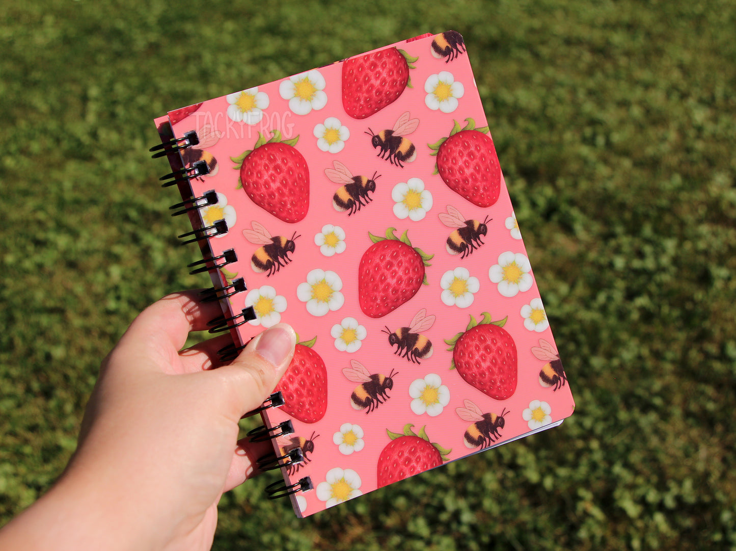 The strawberries and bees-patterned notebook held in a hand.