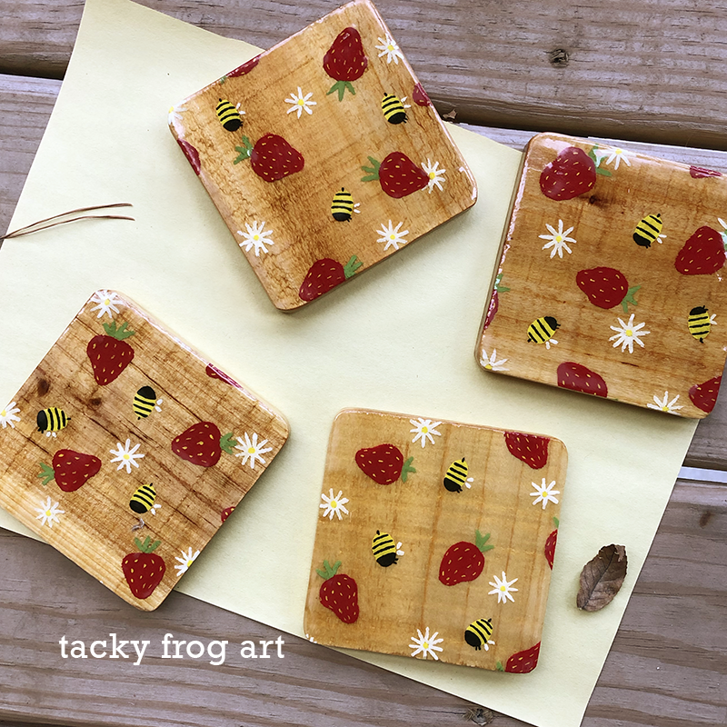 Coasters painted to have strawberries, bees, and daisies on them.
