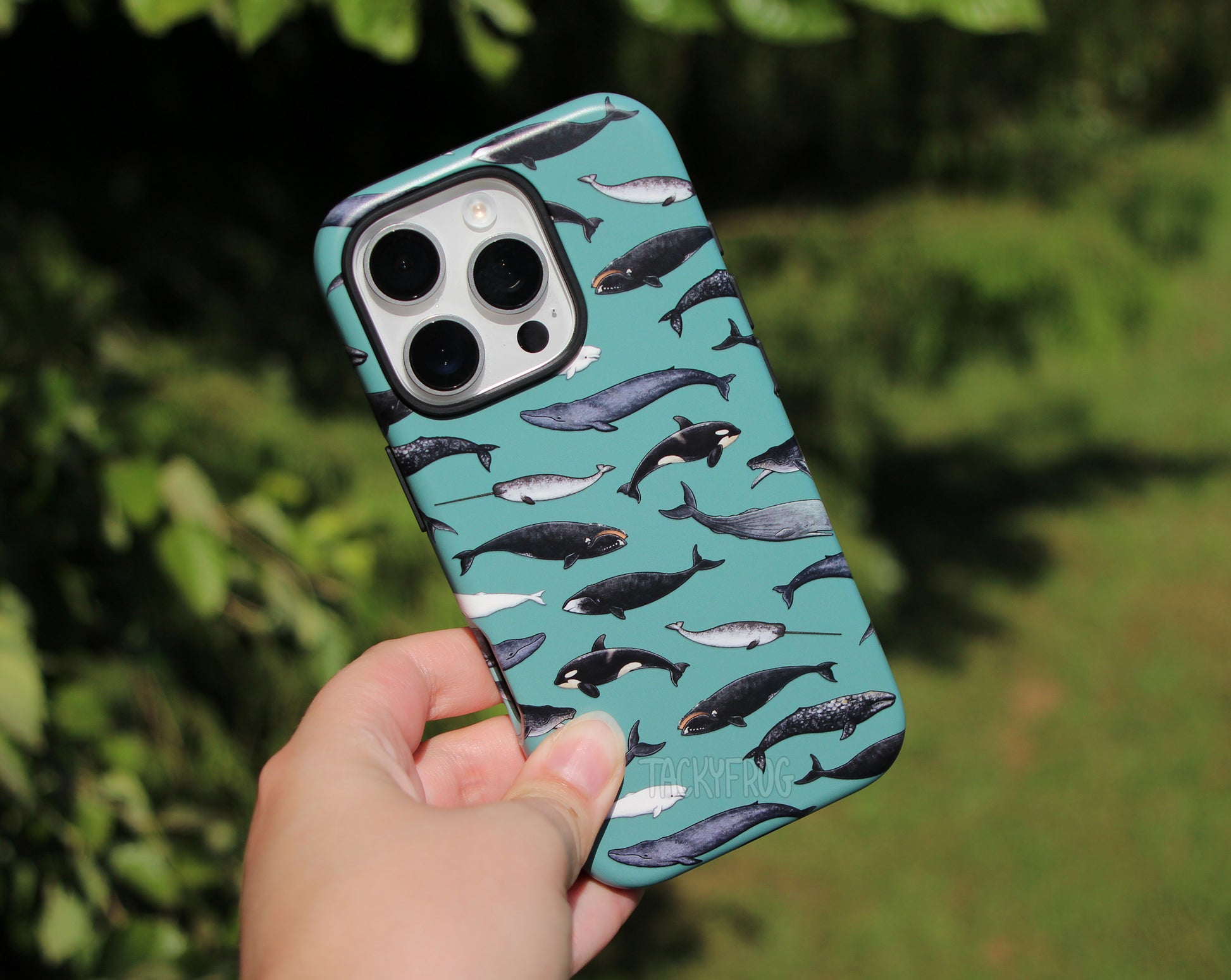 The whale phone case held in front of green vegetation.