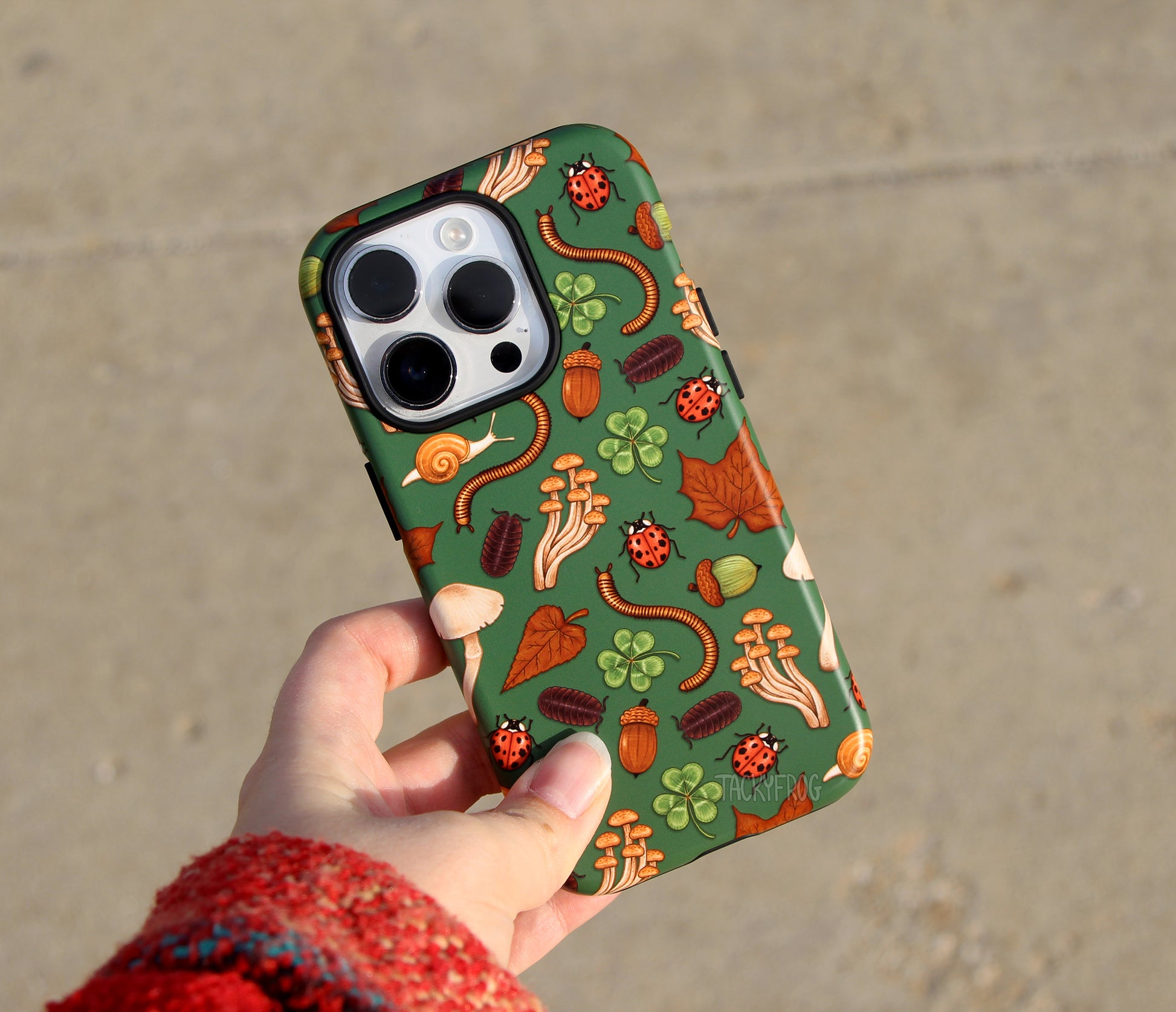 The dark green nature-inspired phone case held above concrete. 