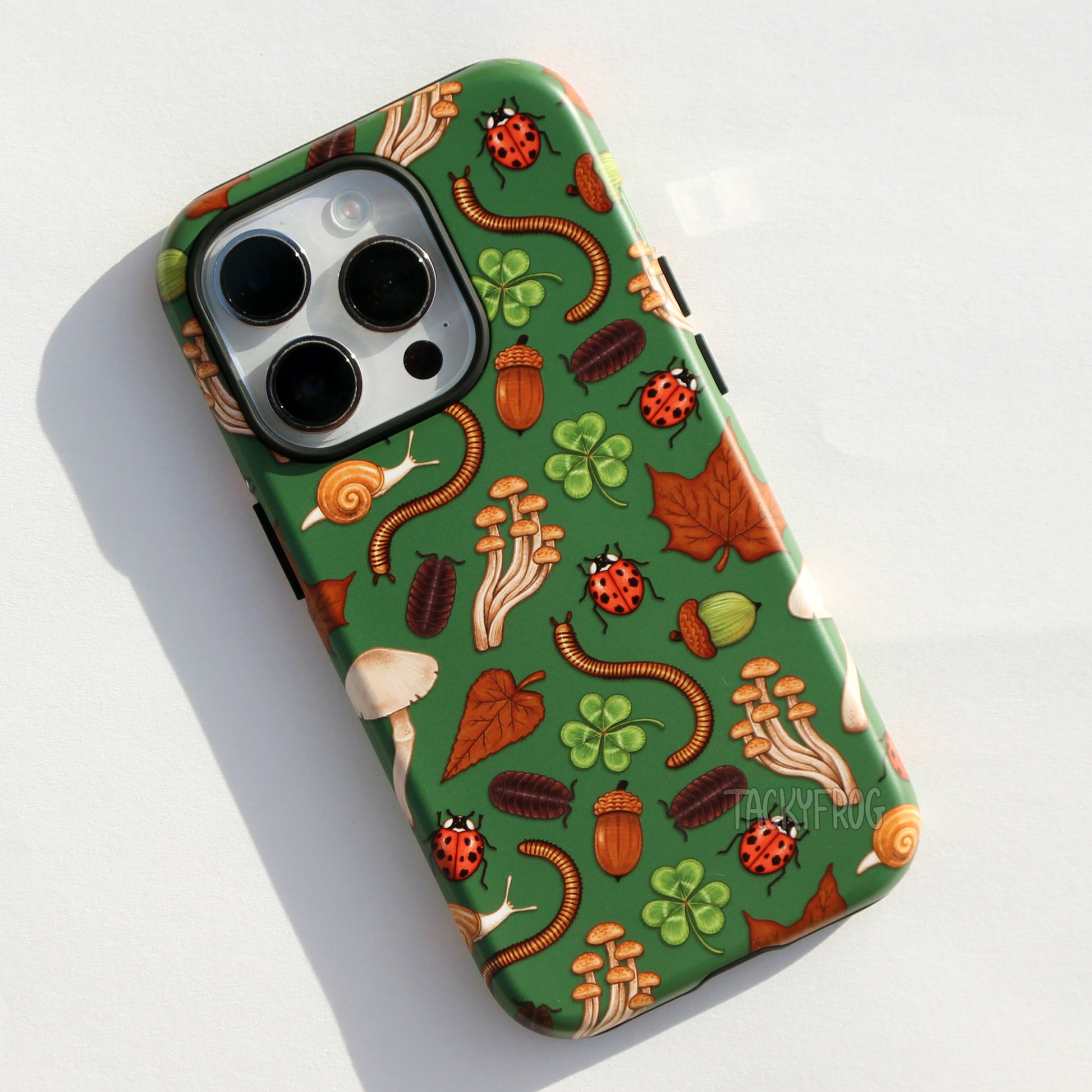 A dark green phone case featuring some common nature objects, specifically dead leaves, mushrooms, acorns, ladybugs, pillbug, millipedes, clovers and snails.