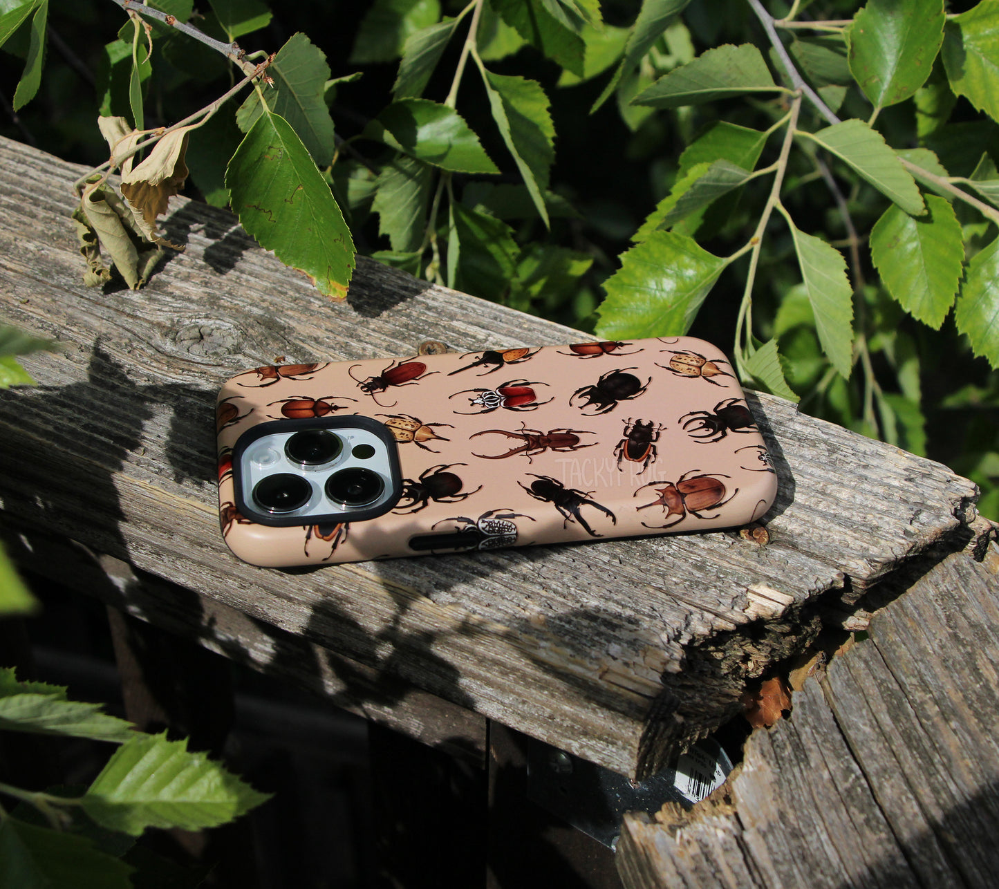 The beetle phone case placed on a wooden railing next to tree branches.