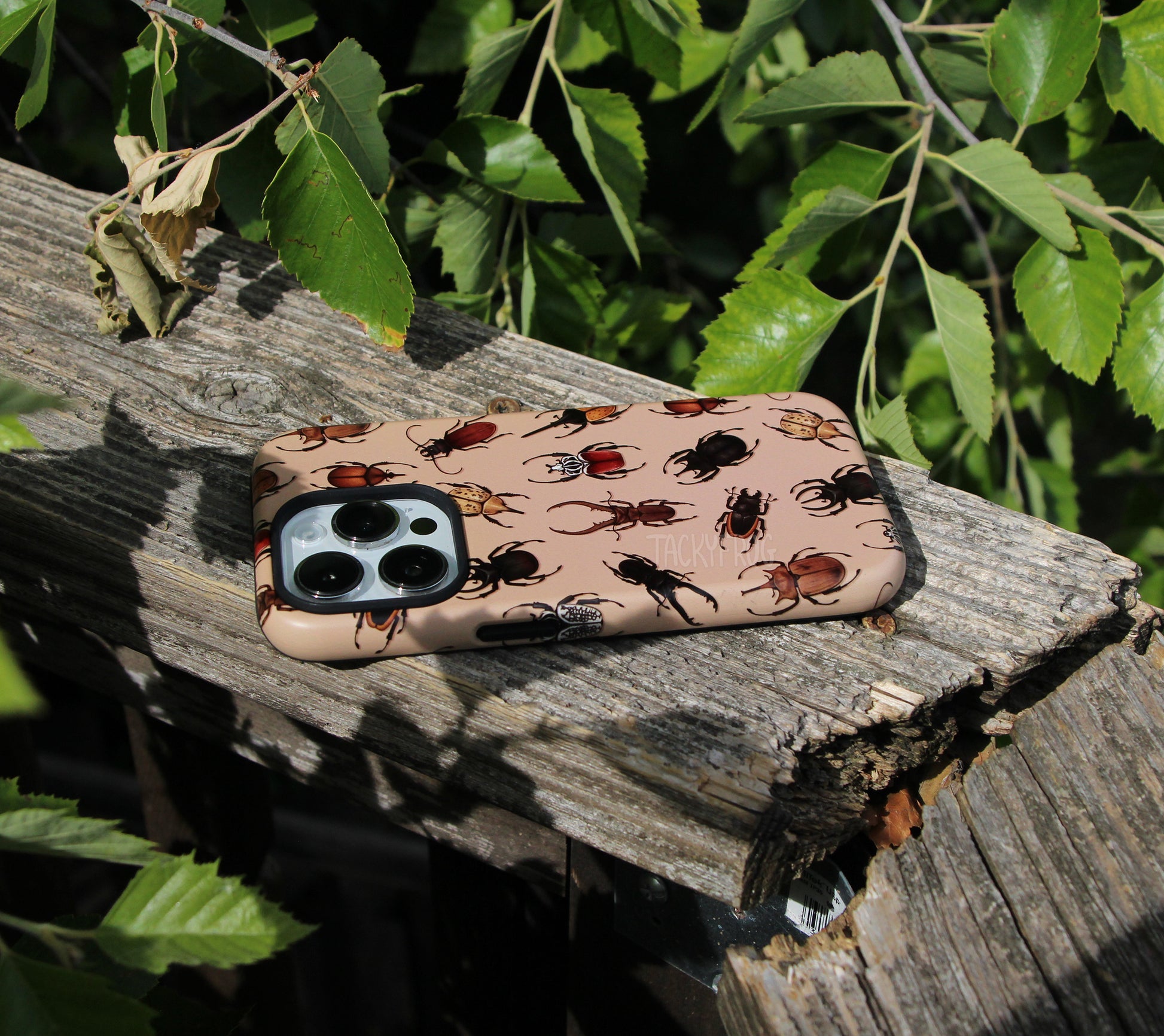 The beetle phone case placed on a wooden railing next to tree branches.