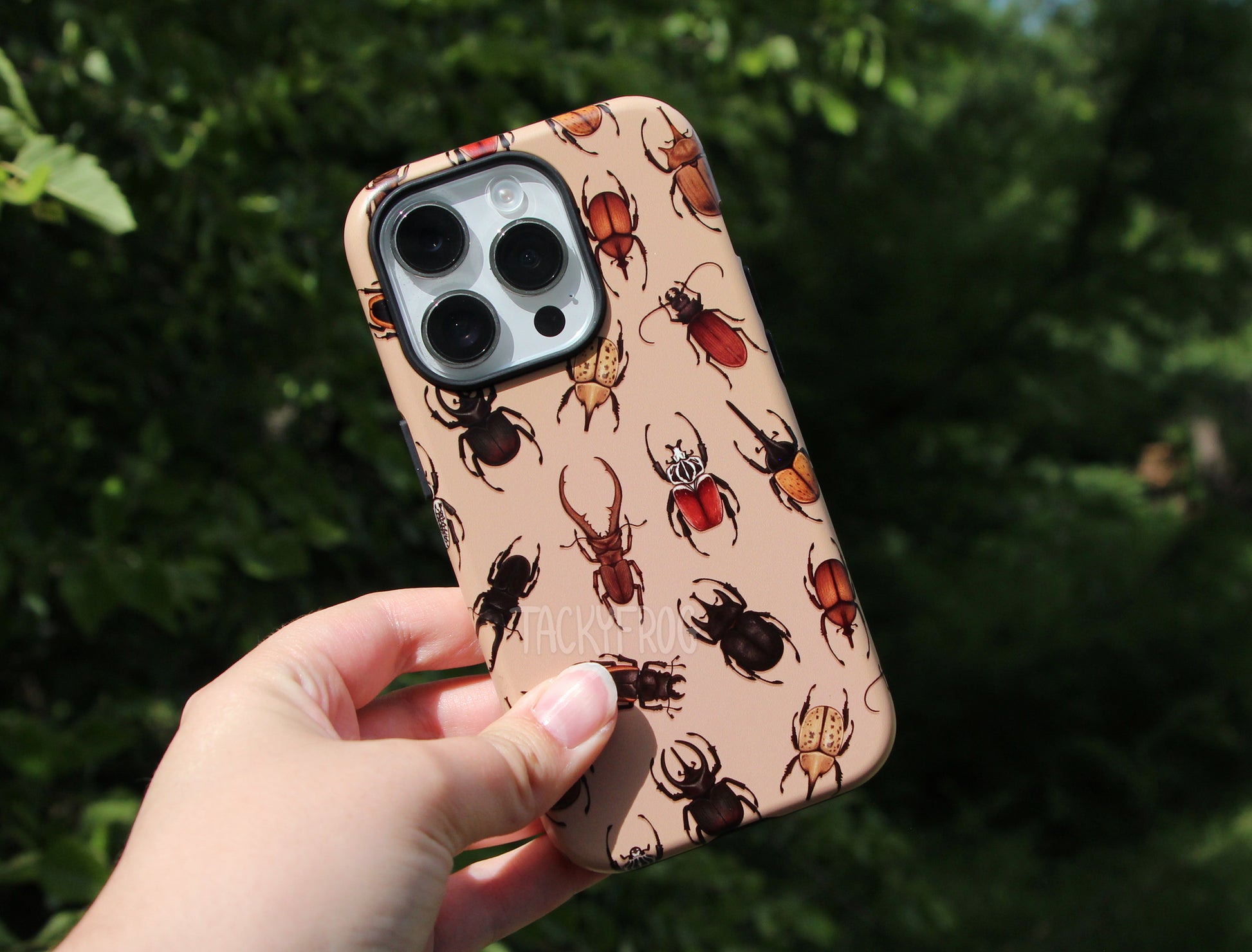 Phone case with beetle design held up against a green leafy background