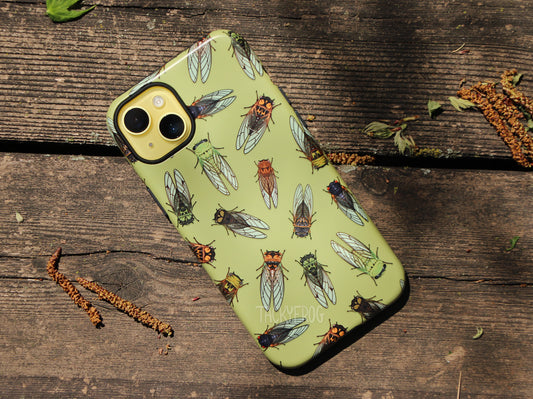 A light green phone case featuring a pattern of cicadas, shown on a yellow phone, placed on a wooden deck.