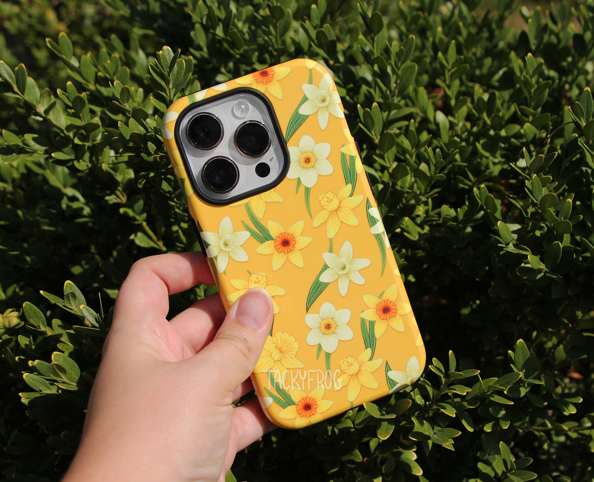 The yellow daffodils tough phone case held over a leafy bush.